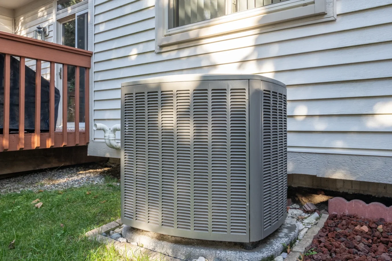 High-efficiency residential air conditioning condenser unit installed outside a home beside a wood deck
