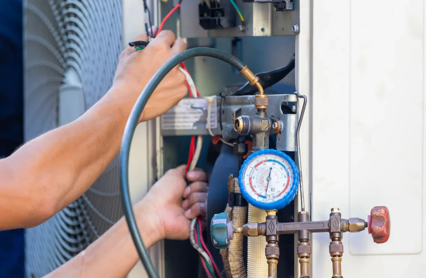 HVAC technician using refrigerant manifold gauges on an AC system